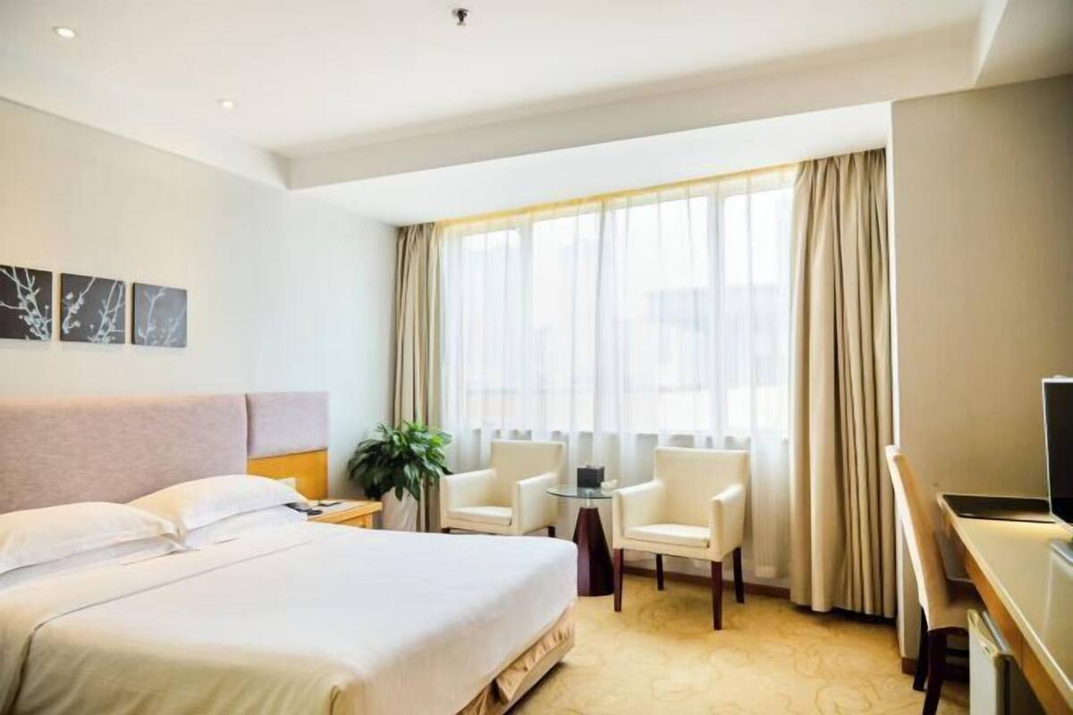 Hotellihuone, jossa on sänky, työpöytä, kaksi tuolia, televisio ja ikkuna, jossa on verhot.