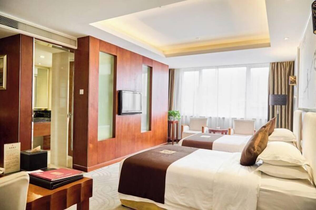 Hotellihuone, jossa on kaksi sänkyä, televisio, työpöytä ja näkymä ulos.