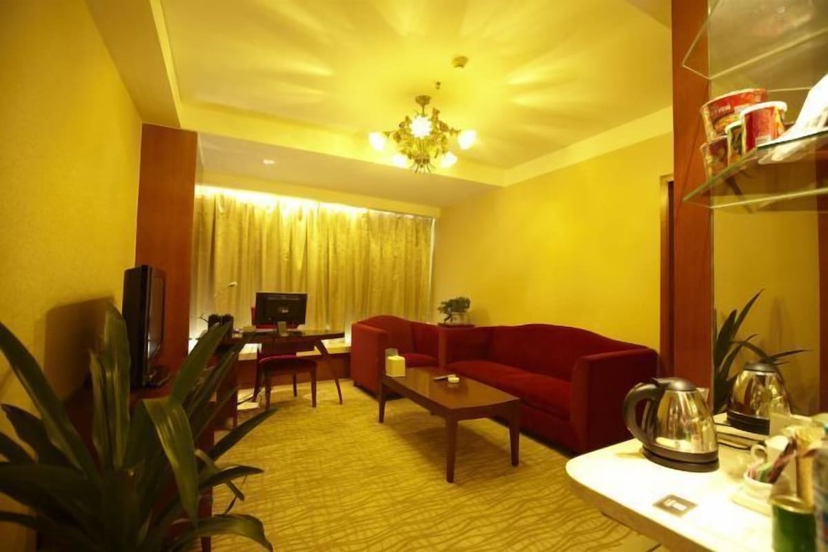 A hotel room with a red sofa, a wooden coffee table, a television, and a large window with curtains.