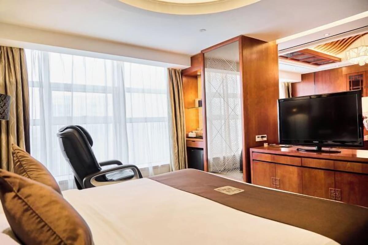 A hotel room with a bed, a desk, a television, and a window with curtains.