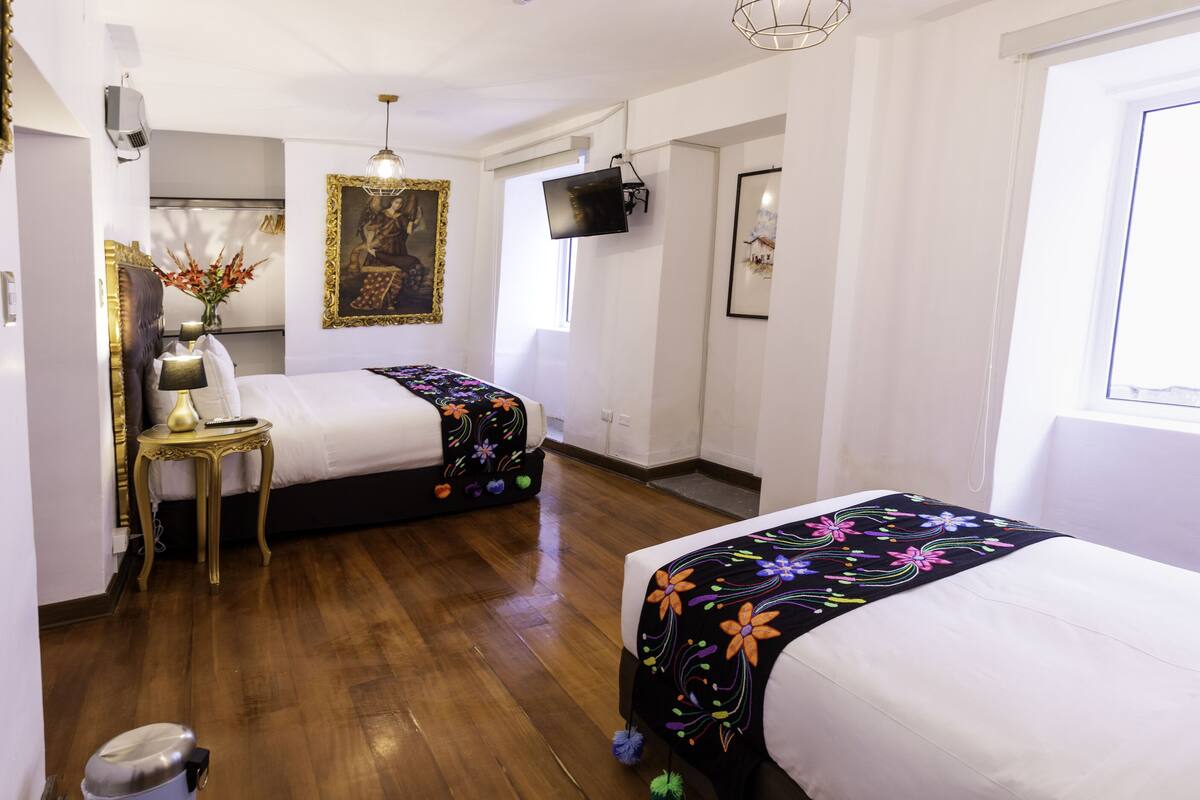 A hotel room with two beds, a desk, a chair, a TV mounted on the wall, and a window.