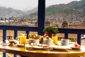A breakfast table with various food items and a view of a cityscape with mountains in the background.