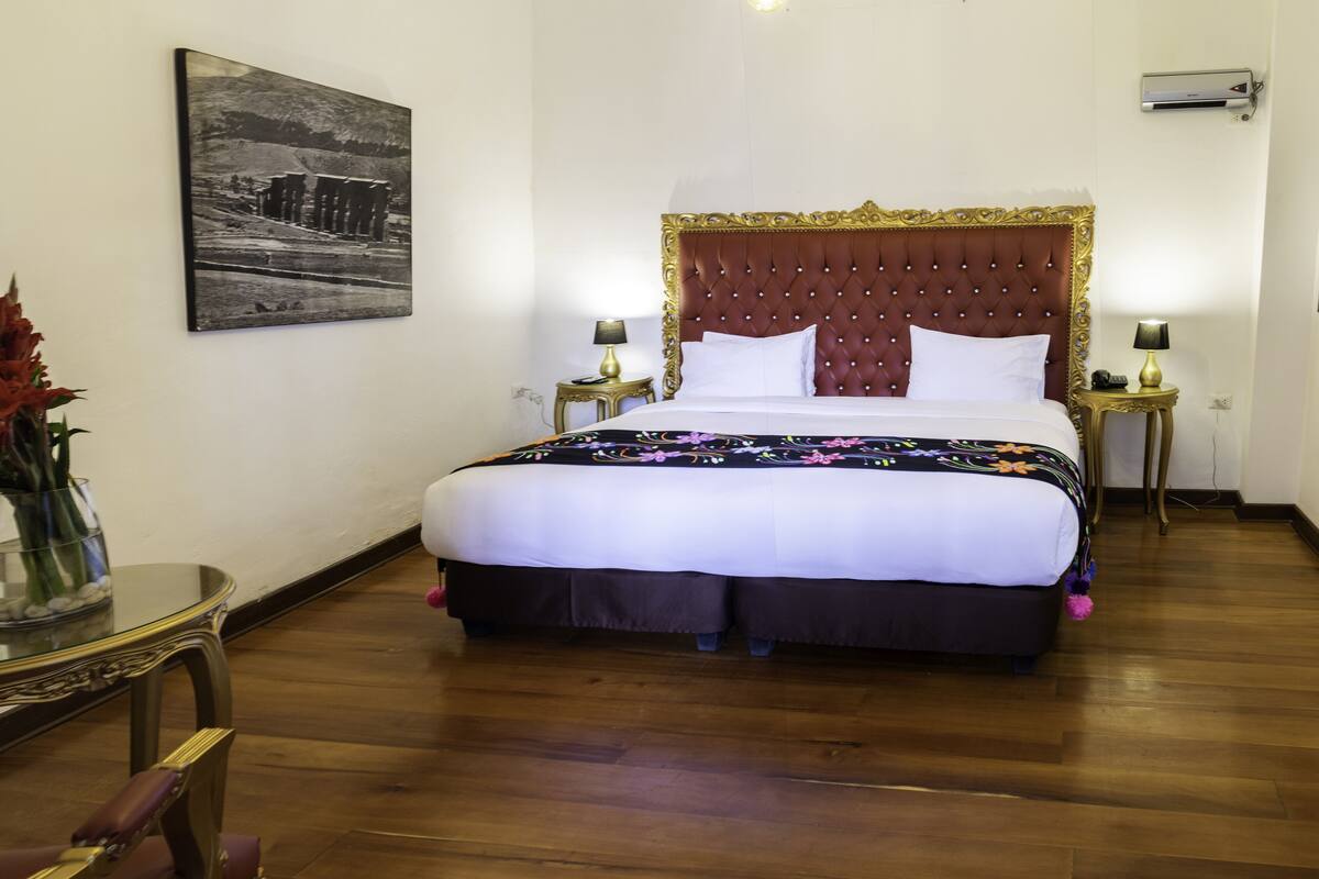 A hotel room with a large bed, a nightstand with a lamp, a small table with a vase of flowers, and a framed picture on the wall.