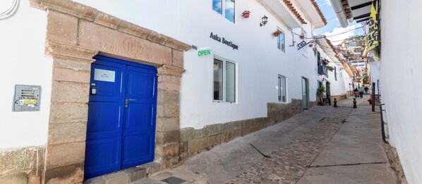 Eine schmale Straße mit einer blauen Tür, einem weißen Gebäude und einem Schild mit der Aufschrift 'AUKA Boutique'.