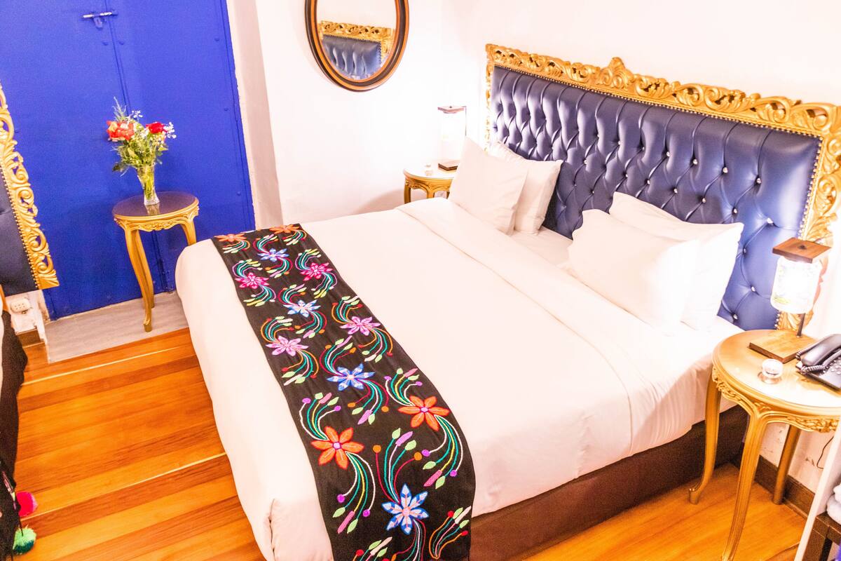 A bed with a floral bedspread, a bedside table with a lamp, and a mirror on the wall.