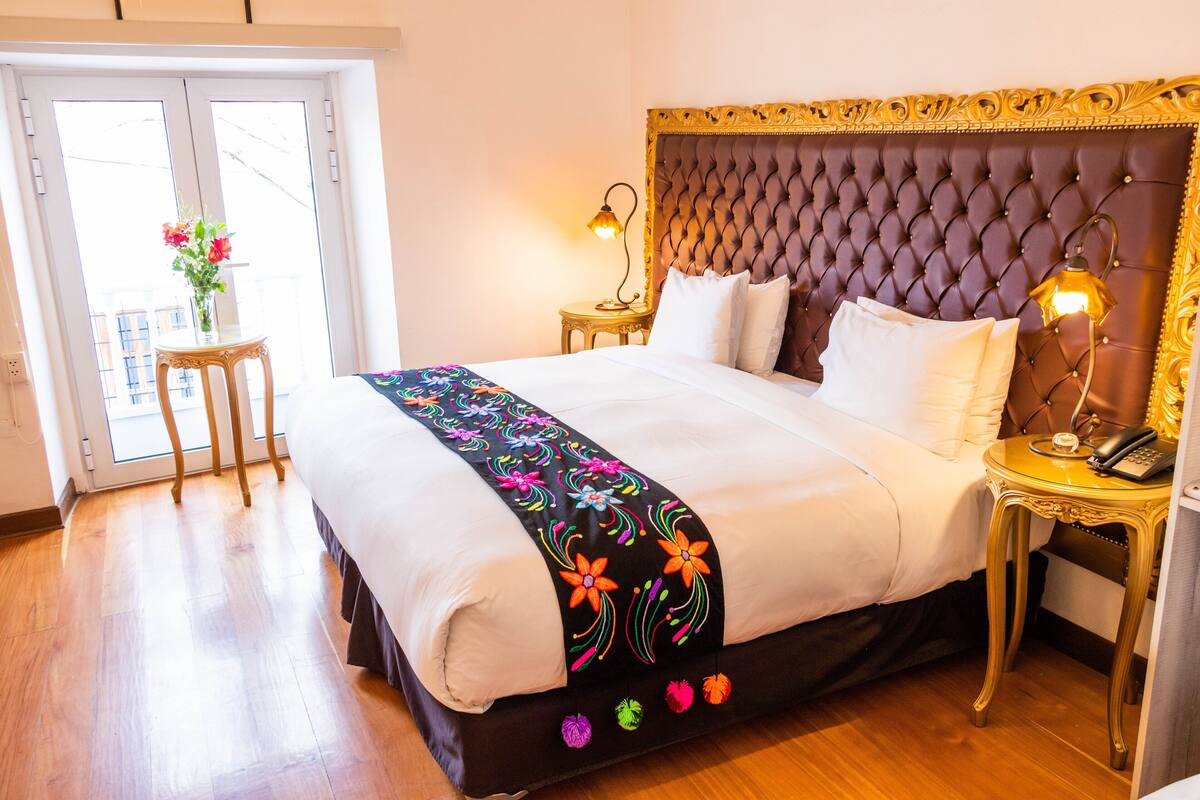 A neatly made bed with a floral bedspread, a tufted headboard, and a bedside table with a lamp and phone.