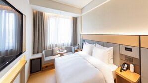 Ein Hotelzimmer mit einem großen Bett, einer Sitzecke, einem kleinen Tisch, einem Fernseher und einem Nachttisch mit Telefon und Lampe.