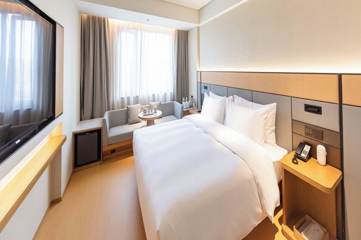 Ein Hotelzimmer mit einem großen Bett, einer Sitzecke, einem kleinen Tisch, einem Fernseher und einem Nachttisch mit Telefon und Lampe.