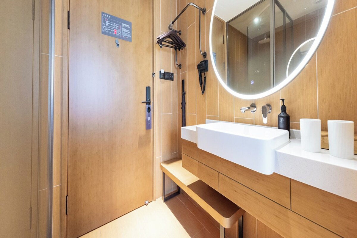 A modern bathroom with a wooden vanity, a large mirror, and a shower area.