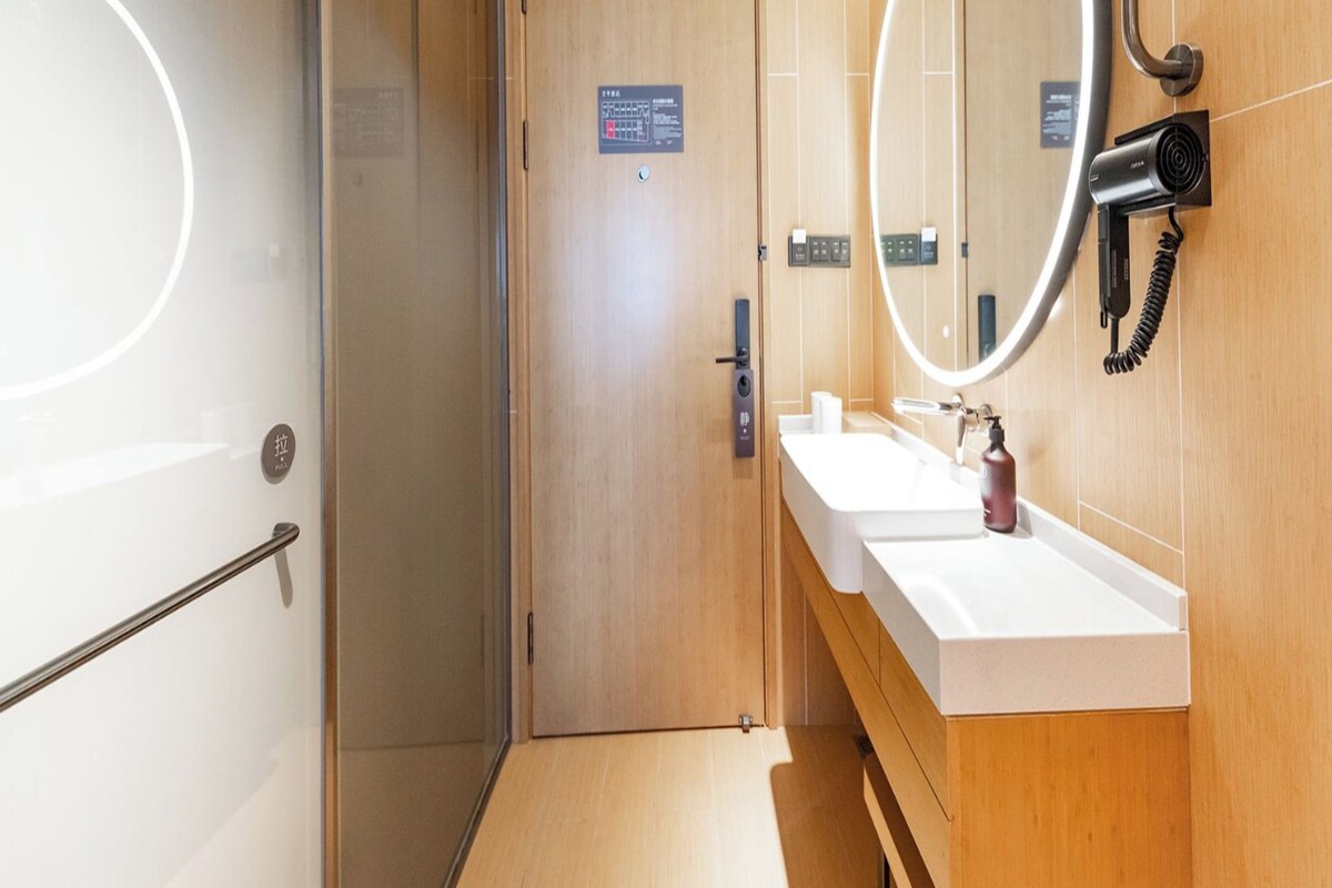 Un baño moderno con cabina de ducha de vidrio, tocador de madera con espejo y perchero.