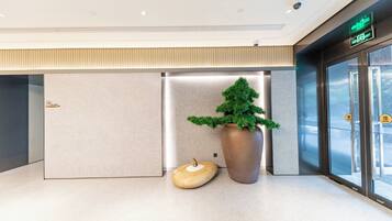 Un vestíbulo moderno con diseño minimalista, que presenta una gran planta en maceta, una escultura de madera original y una puerta de cristal con señal de salida.