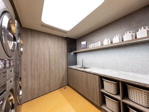 A laundry room with a washing machine, a sink, and shelves with toiletries. - Ji Hotel (Shanghai)