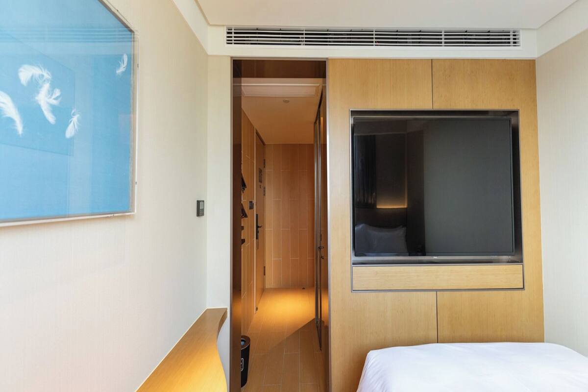 Ein Hotelzimmer mit Bett, Fernseher, Holz-Kopfstück, Duschbereich und Bad mit Toilette und Waschbecken.