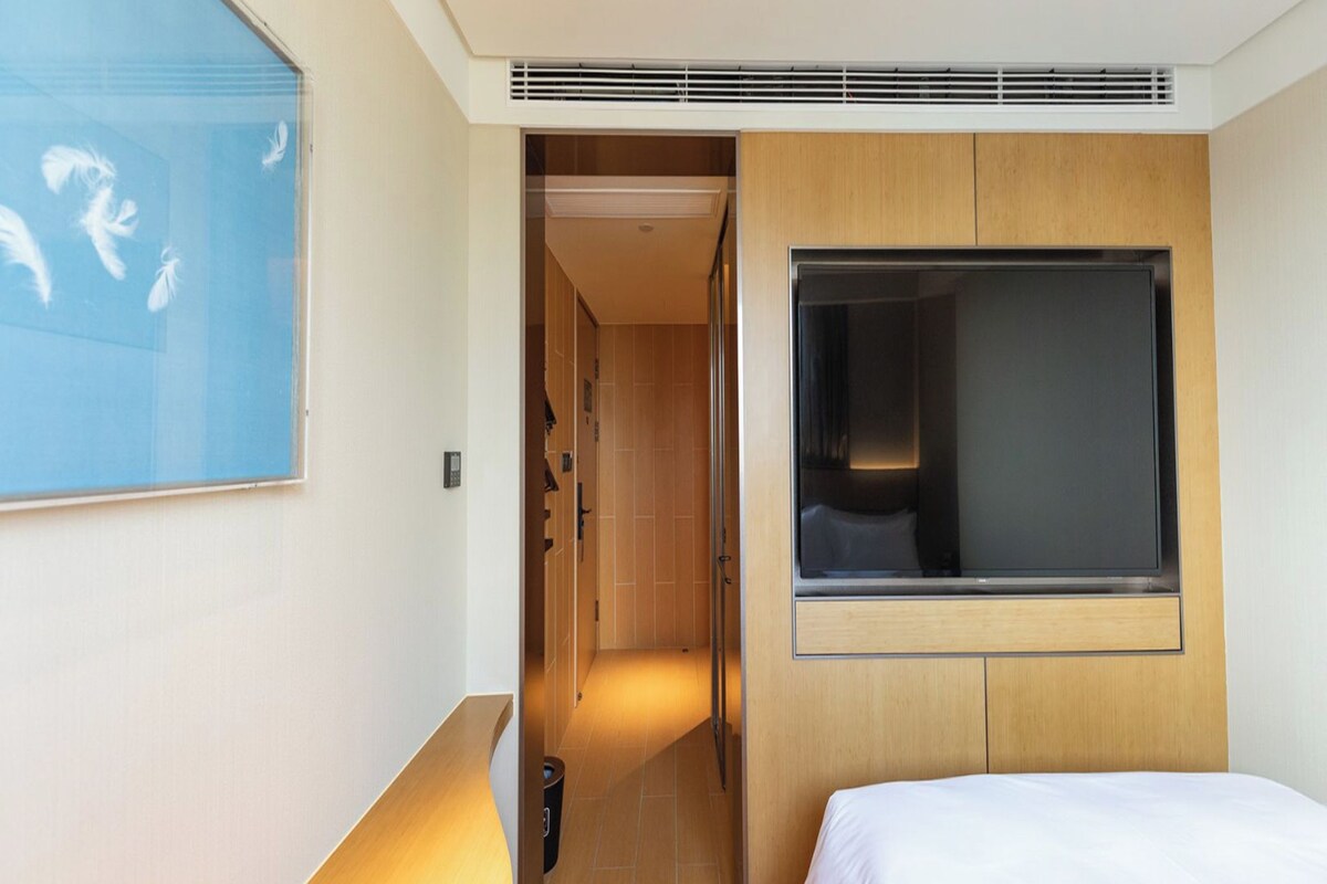 A hotel room with a bed, a TV, a wooden headboard, a shower area, and a bathroom with a toilet and sink.