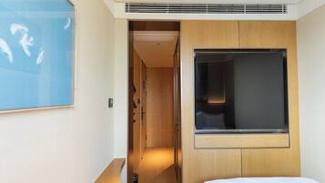 A hotel room with a bed, a TV, a wooden headboard, a shower area, and a bathroom with a toilet and sink.