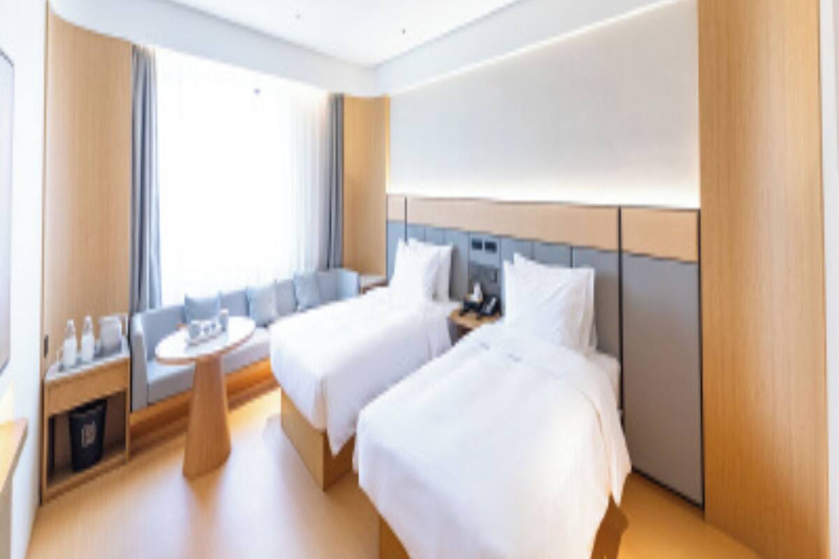 Ein Hotelzimmer mit zwei Betten, einer kleinen Sitzecke und einem Fenster, das natürliches Licht hereinlässt.