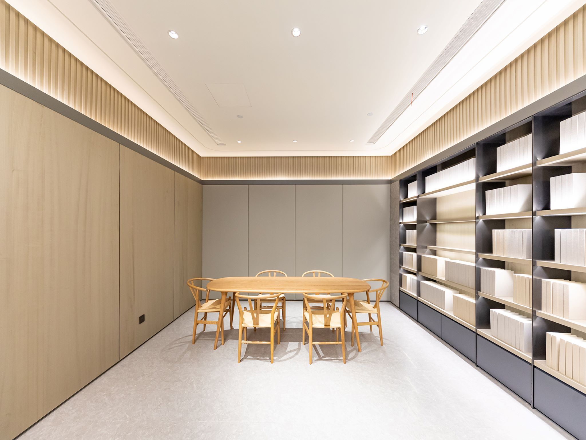 A modern conference room with a wooden table and chairs, a bookshelf, and a neutral color scheme.