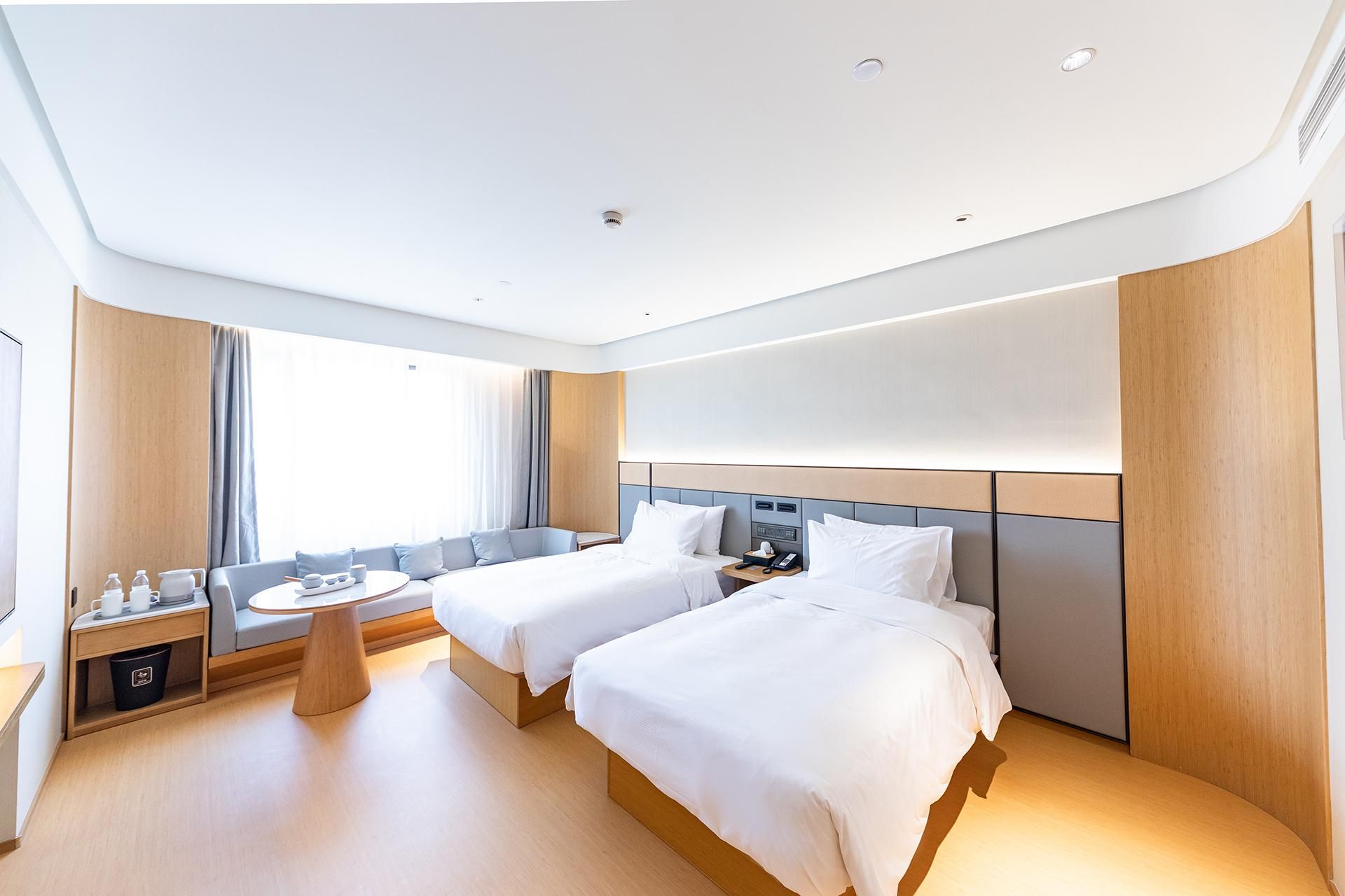 A hotel room with two beds, a bedside table, a small round table, and a window with curtains.