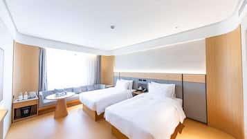 A hotel room with two beds, a bedside table, a small round table, and a window with curtains.