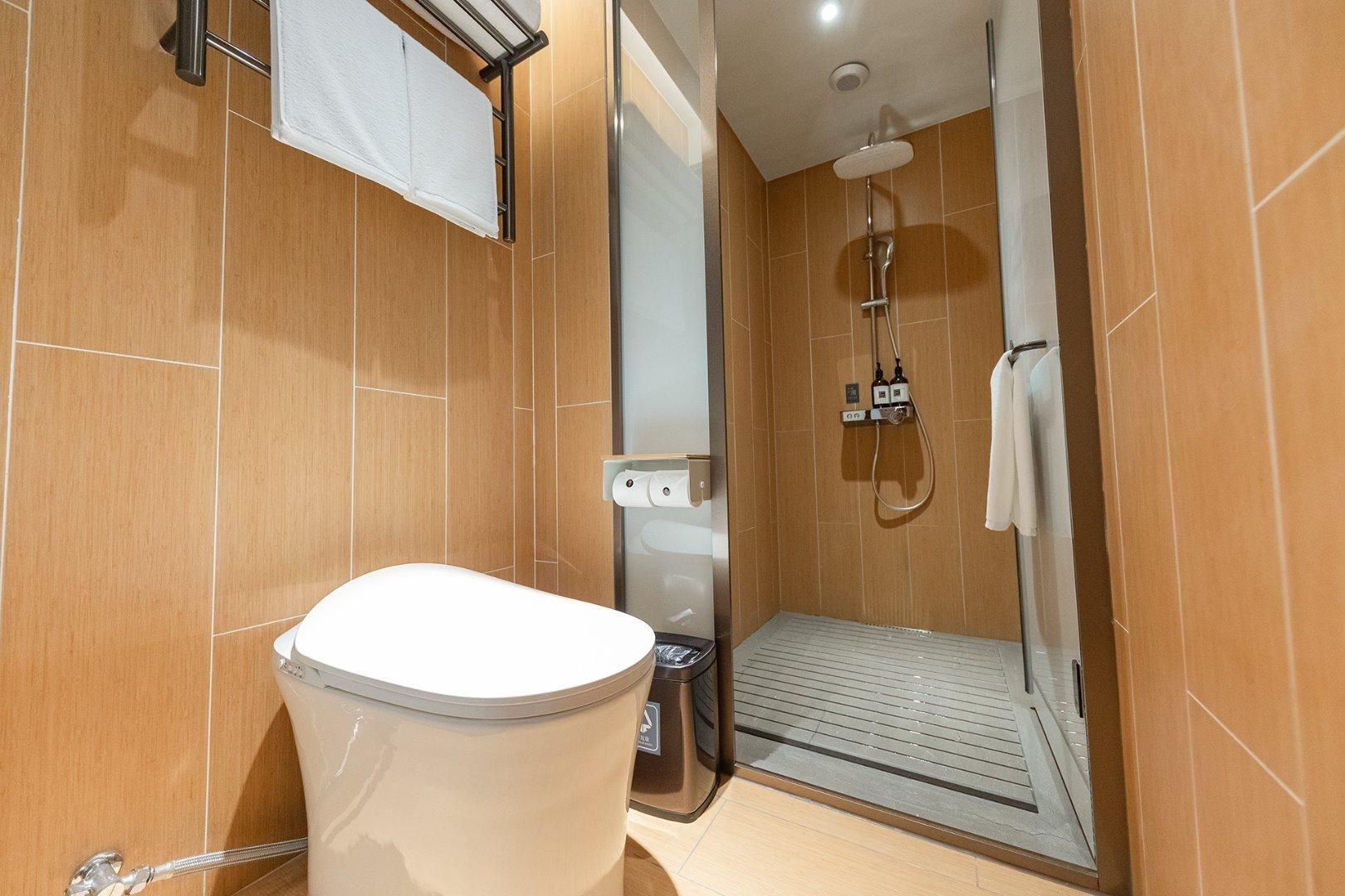 Une salle de bain moderne équipée de toilettes, d’une douche avec une porte en verre et d’un porte-serviettes.