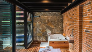 A modern bathroom with a stone wall, a wooden floor, a glass door, and a bathtub. - Matian Hotel Boutique (Tequisquiapan)