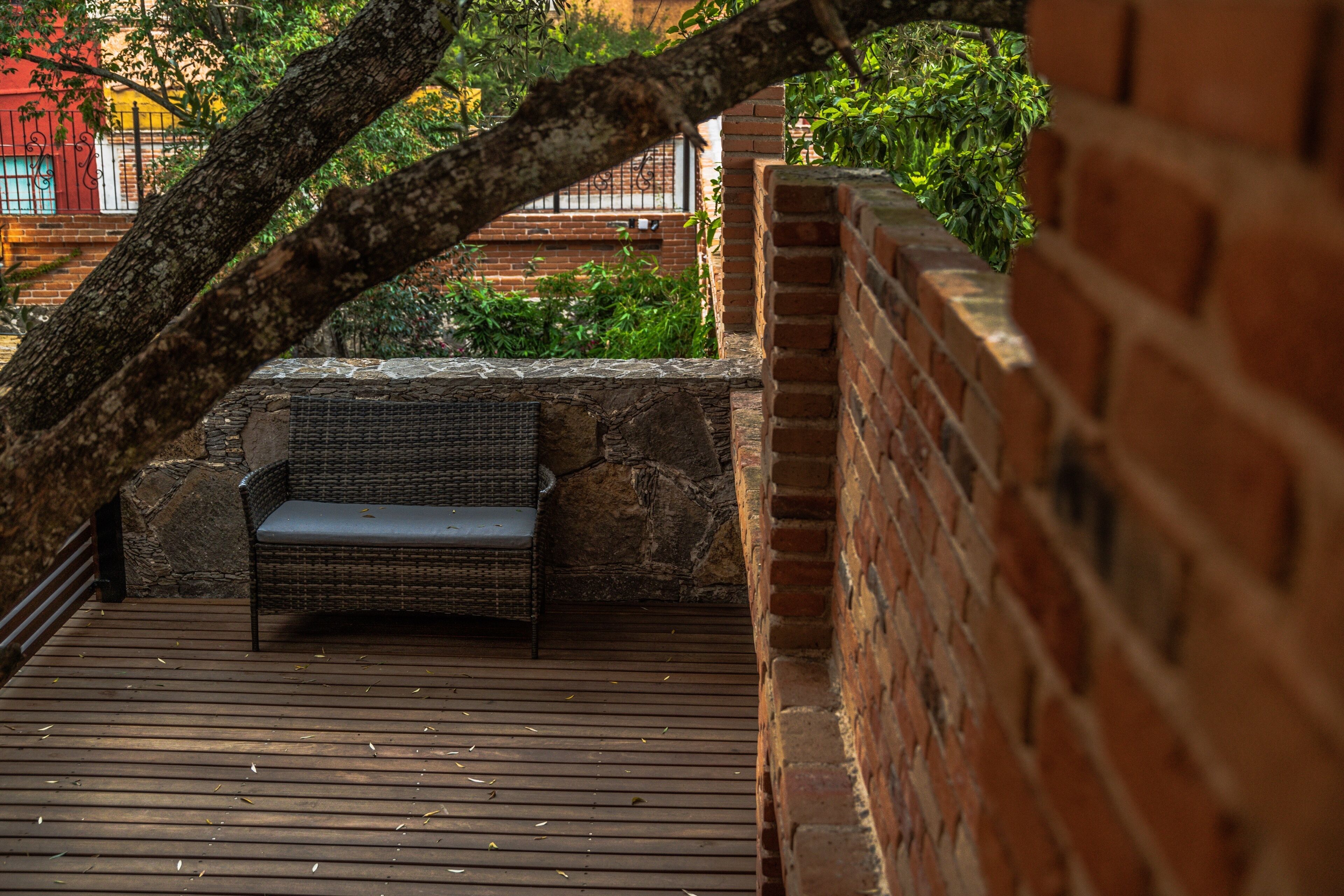 Une terrasse en bois avec un banc en osier, des murs en briques et une vue sur un immeuble à la façade rouge.