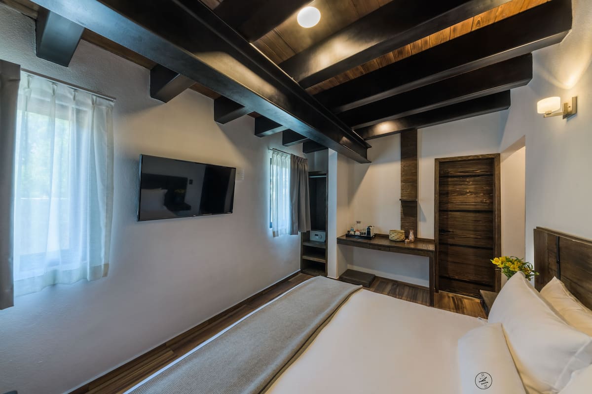 A modern hotel room with a large bed, a flat-screen TV, a wooden ceiling, and a small bathroom area.
