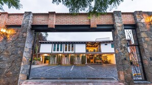 A building entrance with a stone archway, a paved driveway, and a white building with large windows and a balcony. - Matian Hotel Boutique (Tequisquiapan)