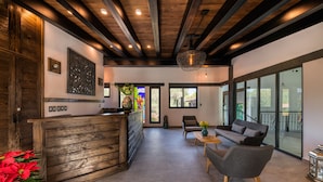 A reception area with a wooden reception desk, a sofa, and a large window offering a view of the outdoors. - Matian Hotel Boutique (Tequisquiapan)
