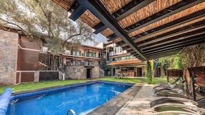 A swimming pool with a stone border, a covered patio area with wooden slats, and a stone building with a staircase. - Matian Hotel Boutique (Tequisquiapan)