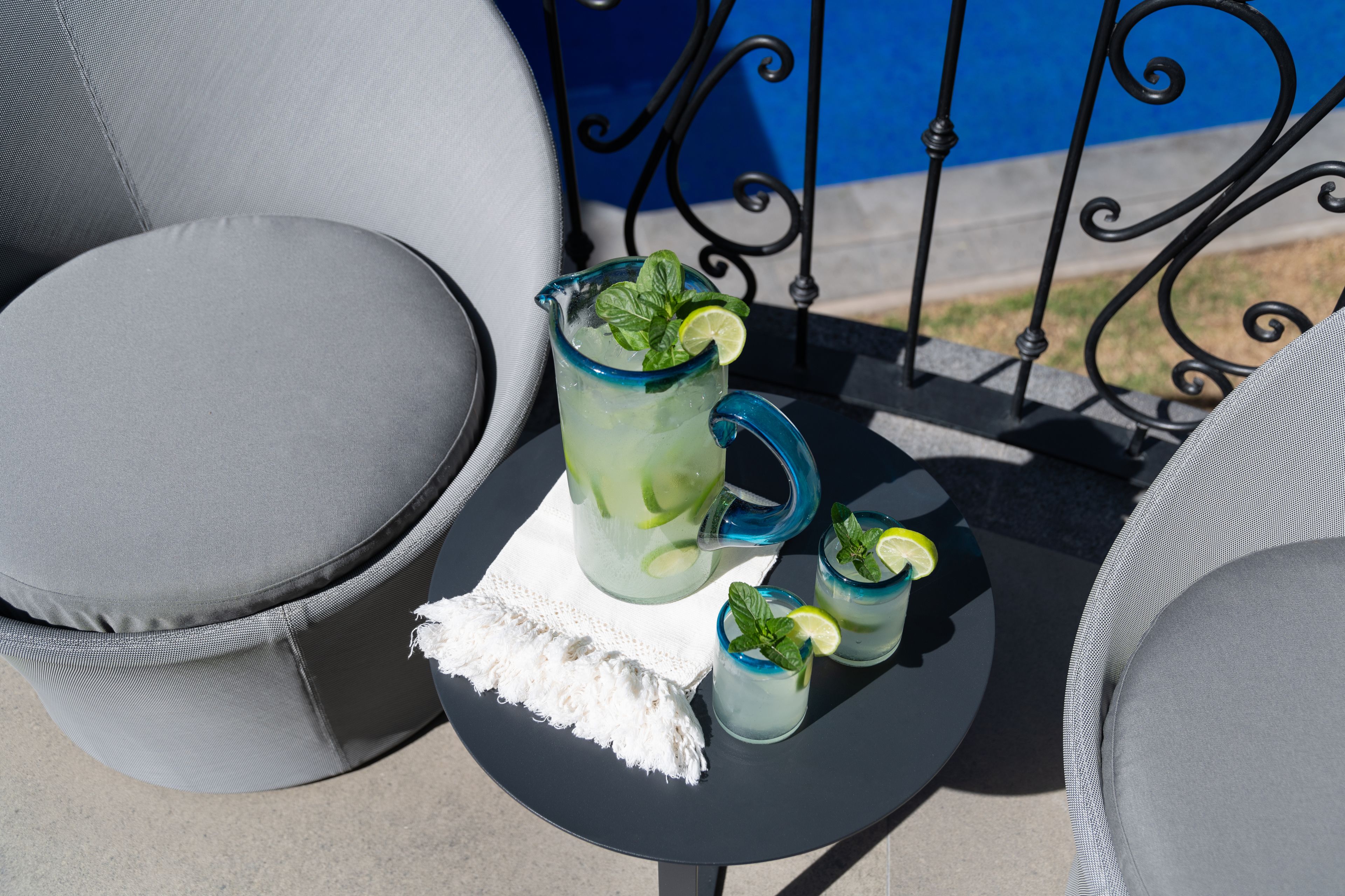 Une table avec une carafe et deux verres contenant une boisson au citron vert, une nappe blanche et des chaises grises.