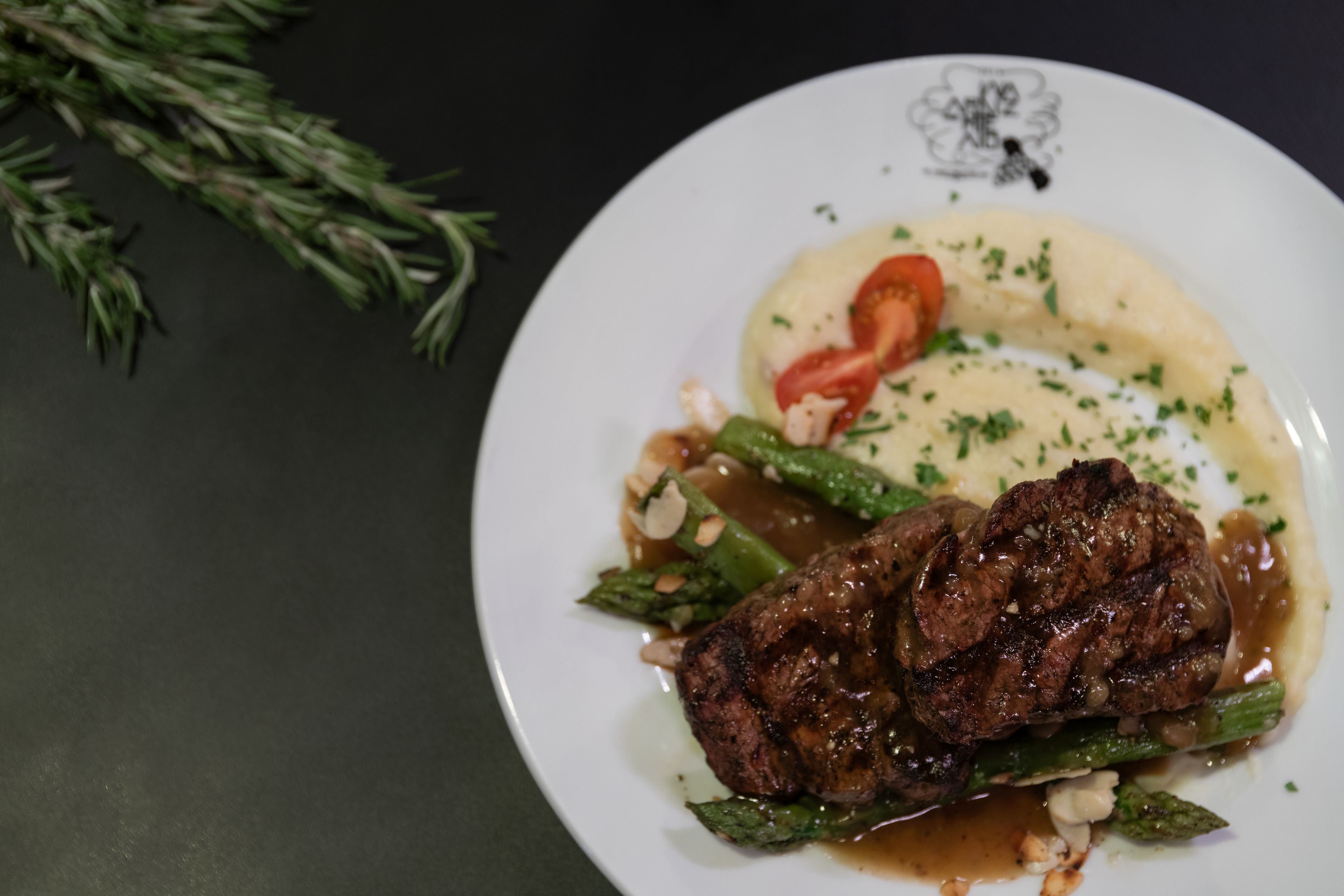 Un plato con un filete, espárragos y puré de papas.