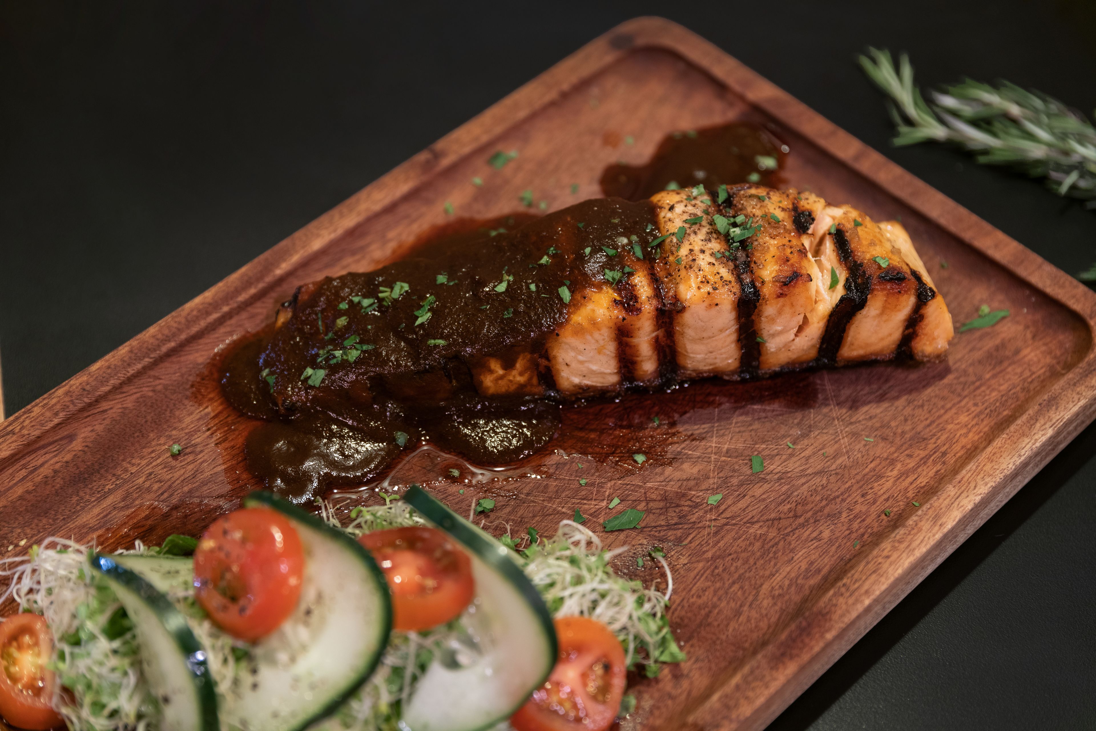 Una tabla de madera con salmón a la parrilla, salsa oscura y una ensalada.