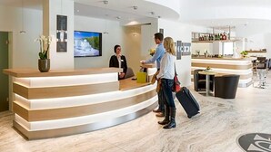 Ein Hotel-Rezeptionsbereich mit einer gebogenen Rezeption, einem Bildschirm und einer Bar mit Sitzgelegenheiten.
