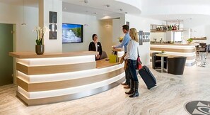 A hotel reception area with a curved reception desk, a TV screen, and a bar area with seating. - Landhotel Kristall (Bad Marienberg)