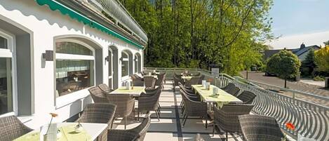 An outdoor cafe with wicker furniture and a white building with green trim.