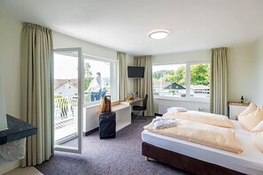 A hotel room with a bed, desk, chair, TV, and a balcony with a view. - Landhotel Kristall (Bad Marienberg)
