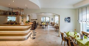 A spacious hotel lobby with a curved bar, multiple dining tables, and a view of the outdoors. - Landhotel Kristall (Bad Marienberg)