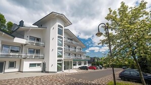 Ein modernes, mehrstöckiges Hotel mit zentralem Eingang, Balkonen und einem Parkplatz.