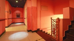 A corridor with a red wall, a tiled floor, and a staircase with a metal railing.