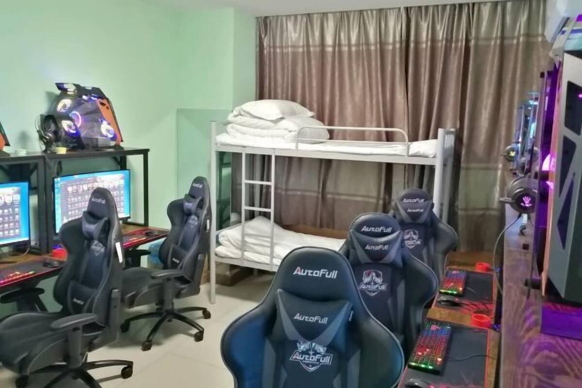 A gaming room with a bunk bed, gaming chairs, multiple monitors, and a desk with a computer.