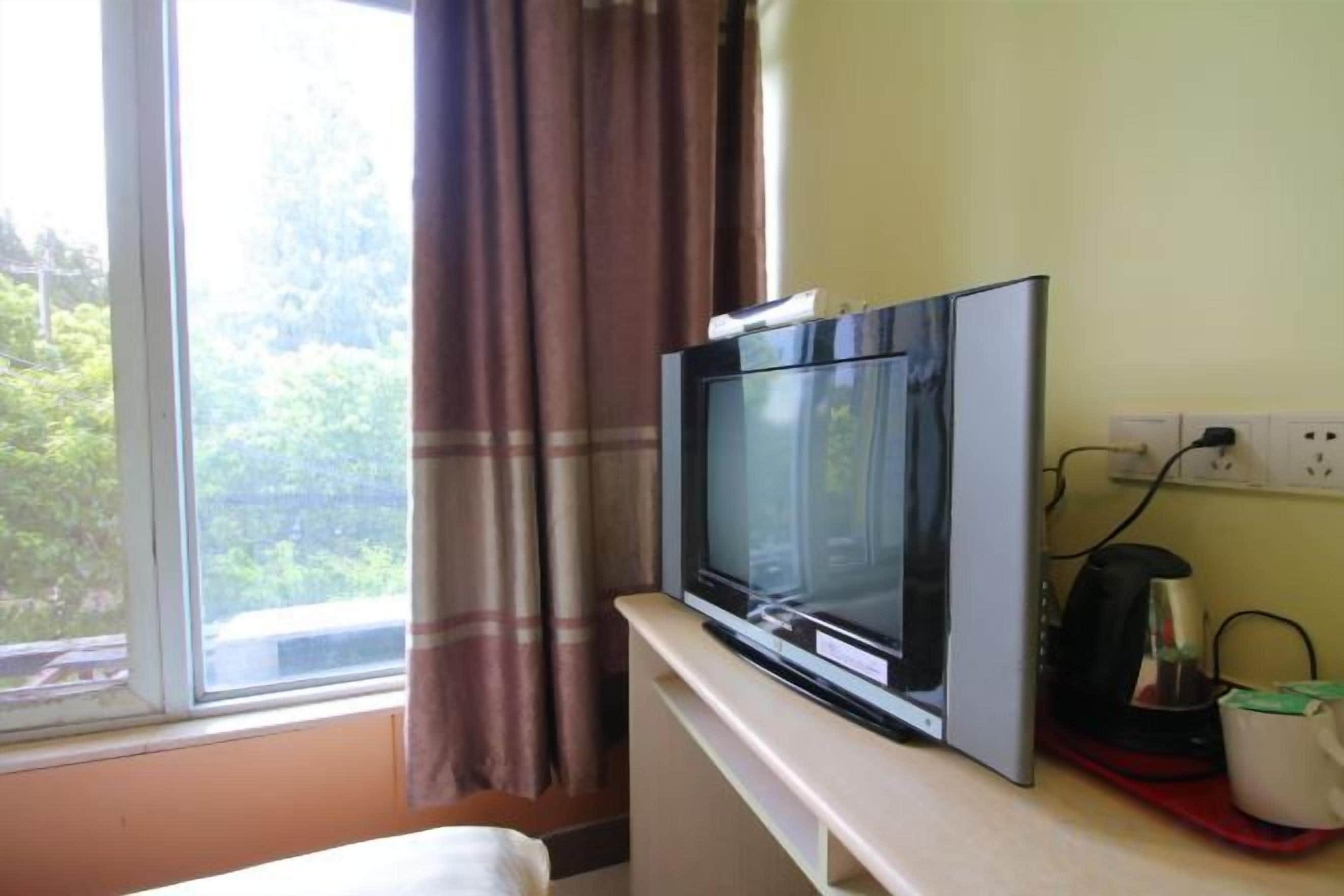 Un televisor sobre un soporte en una habitación con ventana, un enchufe y una cafetera.