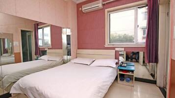 A hotel room with two beds, a window, an air conditioning unit, and a small table with a bowl and a phone.