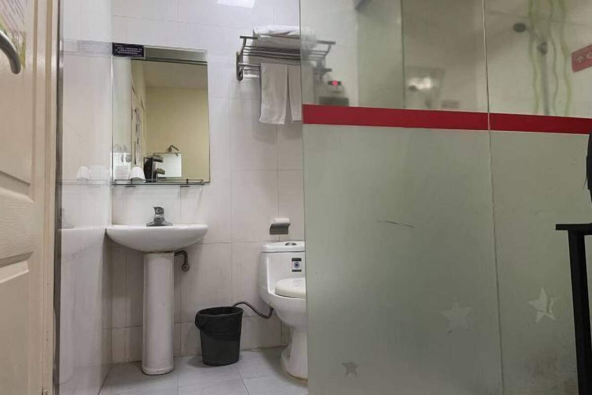 A bathroom with a sink, mirror, toilet, and a trash bin.