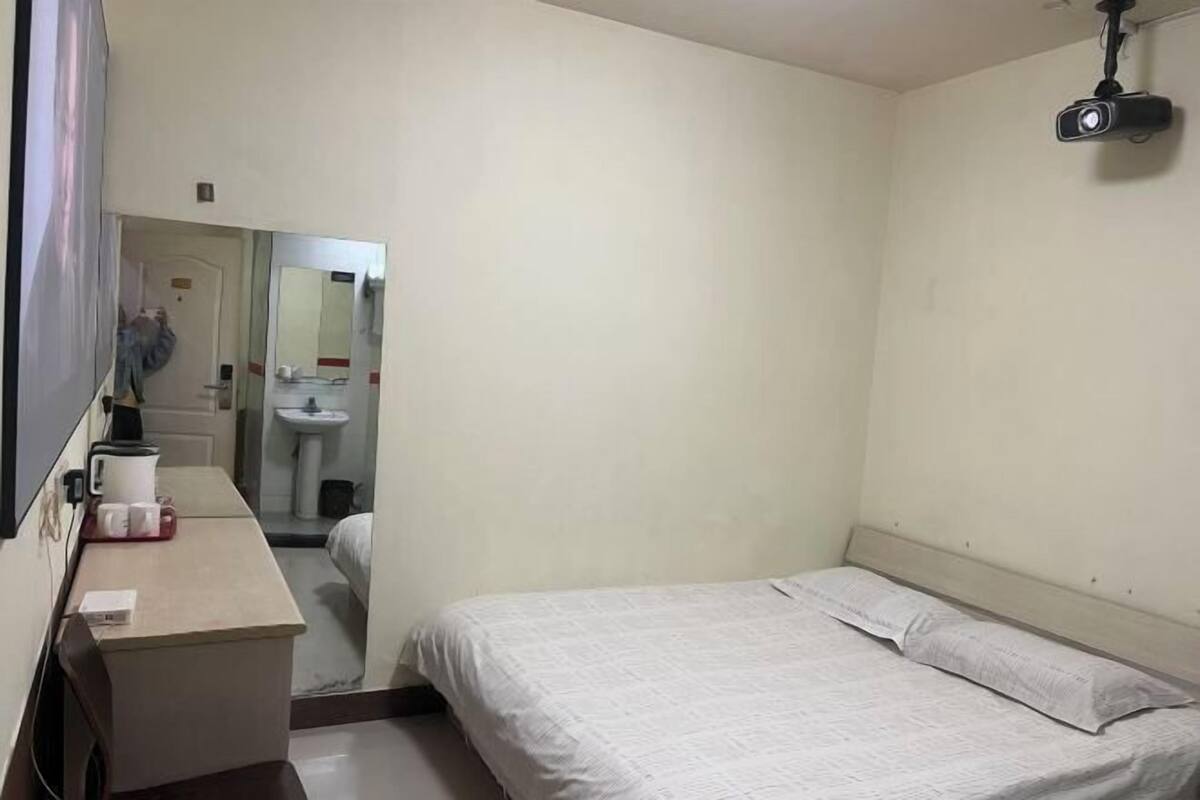 A hotel room with a bed, a desk with a coffee maker, a mirror, and a projector mounted on the wall.