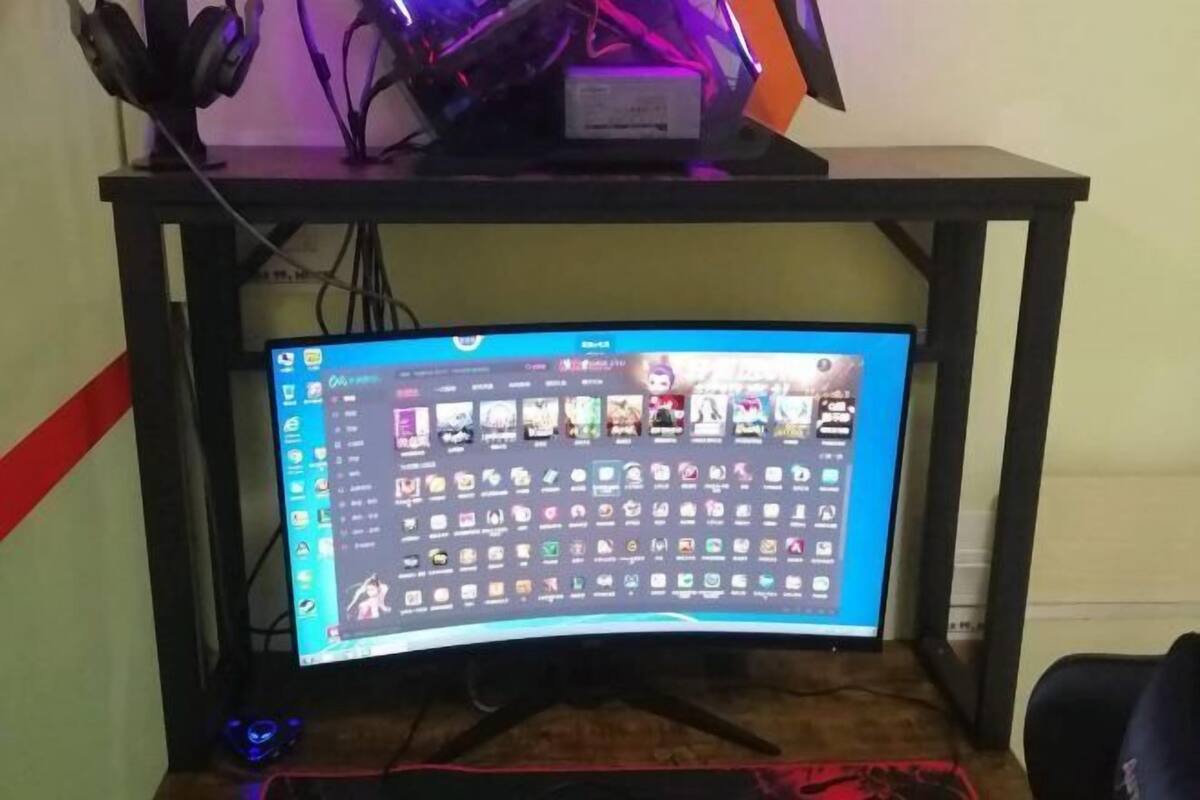 A computer monitor on a desk with a gaming chair, a pair of headphones, and a small blue object on the desk.
