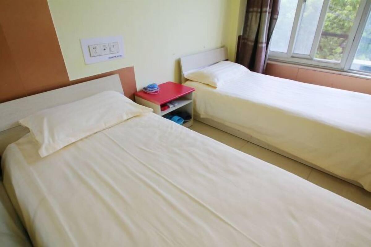 A room with two beds, a red nightstand, a power outlet, and a window with curtains.
