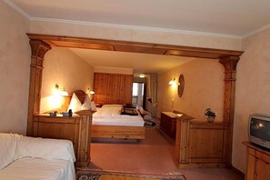 A hotel room with a wooden bed, bedside tables, a television, and a small plant.