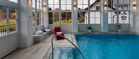 An indoor swimming pool with a clear view of the outside through large windows.