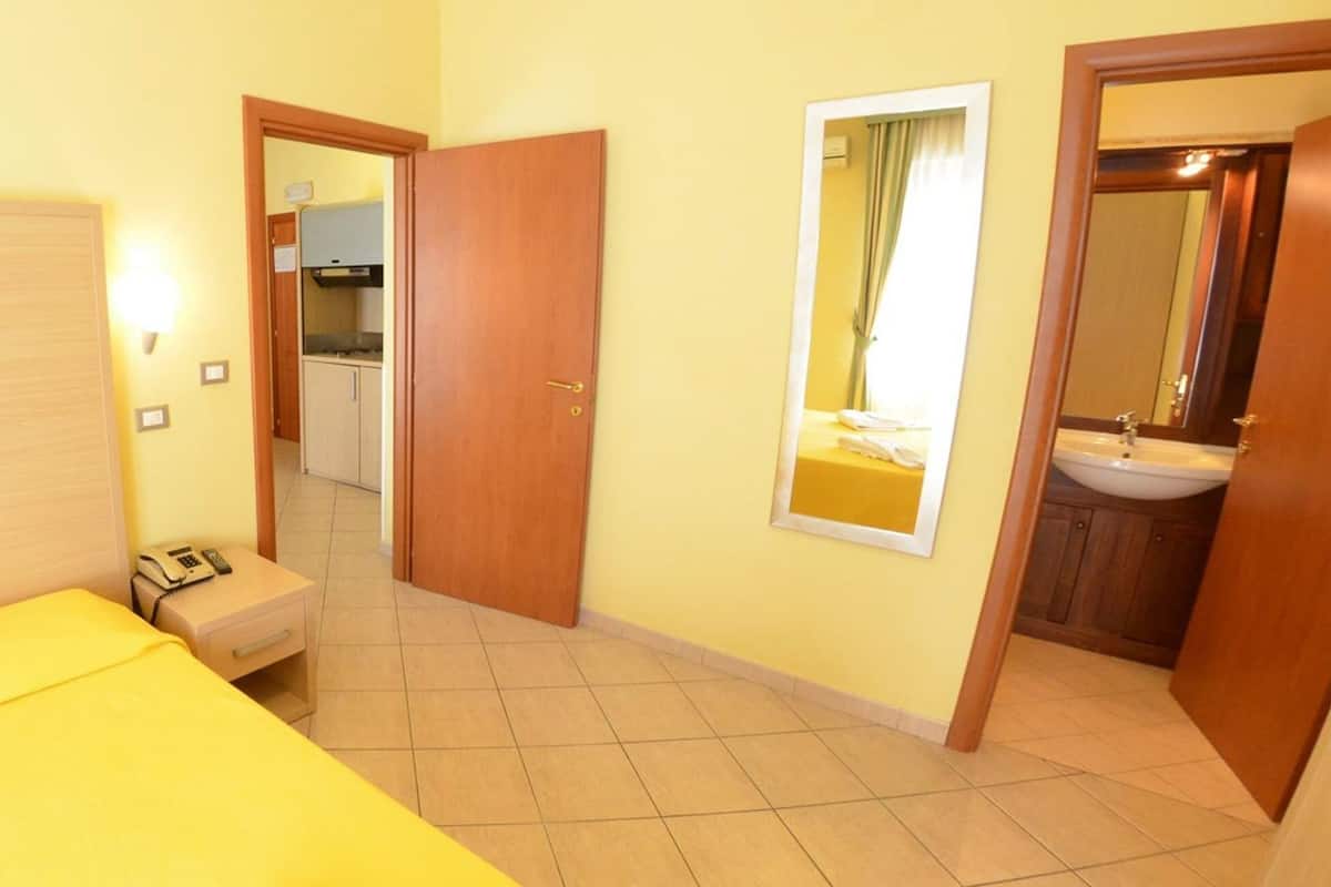 Habitación de hotel con cama, mesita de noche con teléfono, espejo y puerta que da a un baño.